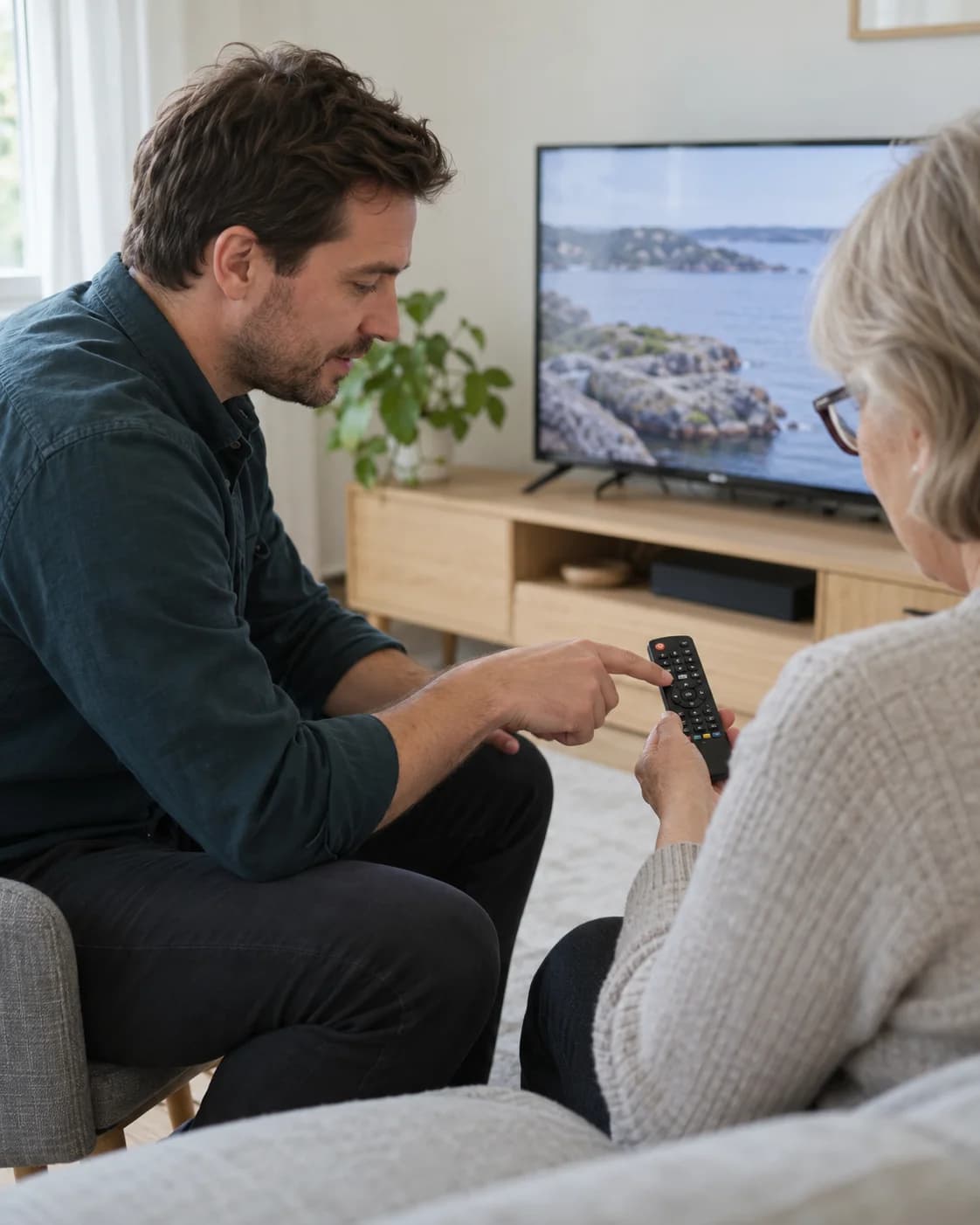 En tekniker visar en äldre person hur TV:ns fjärrkontroll fungerar hemma